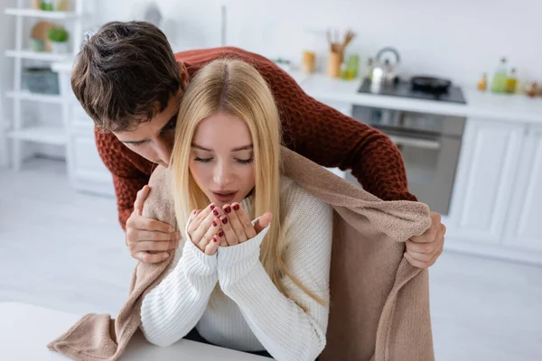 Caring boyfriend in sweater holding blanket near freezing blonde girlfriend — Stock Photo