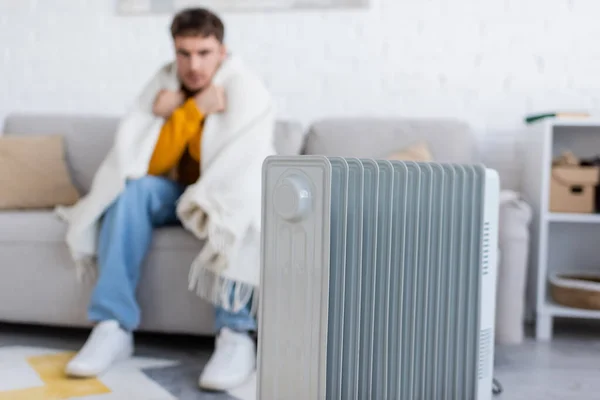 Radiateur chauffe près de l'homme flou couvert de couverture assis sur le canapé dans le salon — Photo de stock