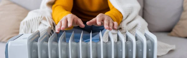 Cropped view of young man covered in blanket sitting on sofa and warming up near radiator heater, banner — Stock Photo