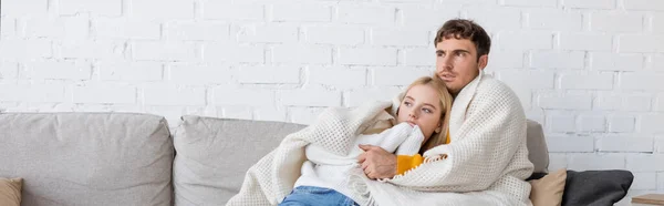Junger Mann umarmt Freundin in Decke gehüllt und sitzt im Wohnzimmer, Banner — Stockfoto