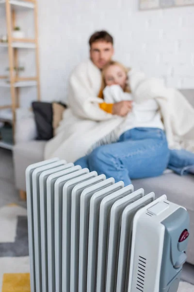 Aquecedor radiador moderno perto de abraços casal borrado e sentado no sofá sob cobertor — Fotografia de Stock