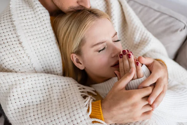 High angle view of man covered in blanket kissing head of blonde woman in white sweater warming up hands — Stock Photo