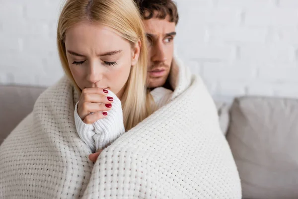 Blonde woman in white sweater warming up hands near boyfriend covered in blanket — Stock Photo