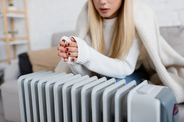 Vue recadrée de la jeune femme blonde couverte de couvertures chauffantes mains près du radiateur — Photo de stock