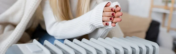 Cropped view of young woman covered in blanket warming hands near radiator heater, banner — Stock Photo