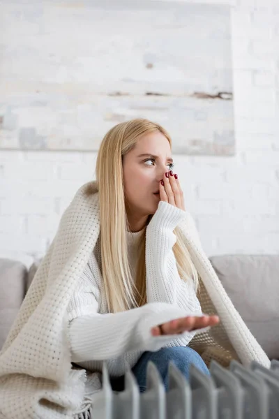 Jovem mulher loira coberta de cobertor mão de aquecimento perto do aquecedor do radiador — Fotografia de Stock