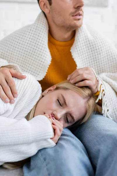 Jeune femme couverte de couverture dormant sur les jambes du petit ami en jeans assis sur le canapé — Photo de stock