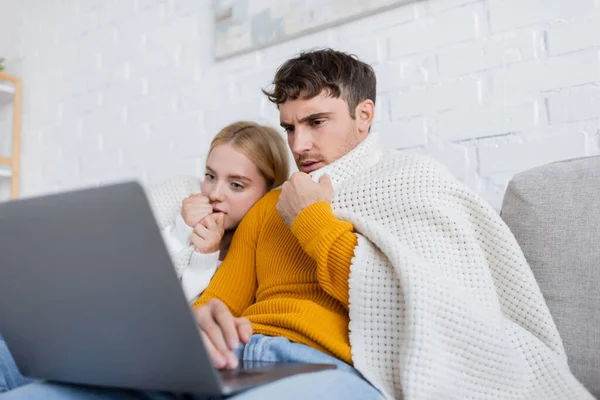 Couple couvert dans couverture regarder film effrayant sur ordinateur portable dans le salon — Photo de stock