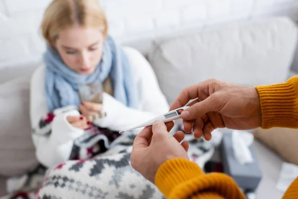 Man holding digital thermometer near blurred and sick girlfriend — Stock Photo