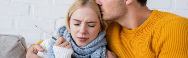 Homme étreignant et embrassant la tête de femme blonde malade avec thermomètre numérique, bannière — Photo de stock