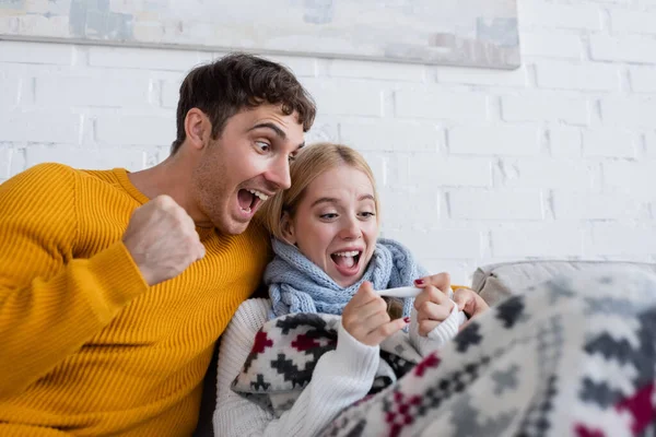 Excited man and sick blonde woman looking at digital thermometer — Stock Photo