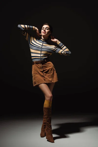 Full length of pretty young woman in striped turtleneck with skirt and boots posing on black — Stock Photo