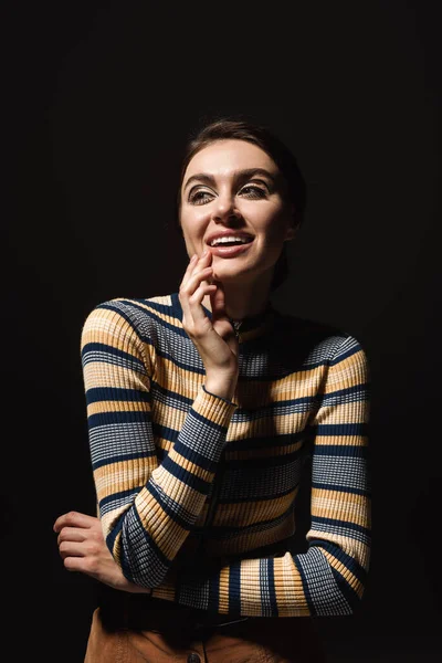 Happy young woman in striped turtleneck looking away isolated on black — Stock Photo