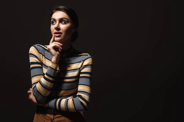 Dreamy young woman in striped turtleneck looking away isolated on black — Stock Photo