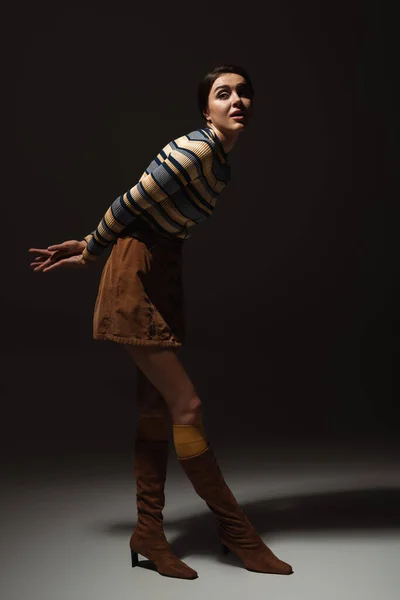 Full length of young model in striped turtleneck with skirt and boots posing on black — Stock Photo