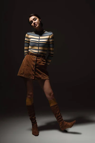 Full length of young woman in turtleneck with skirt and autumnal boots posing on black — Stock Photo