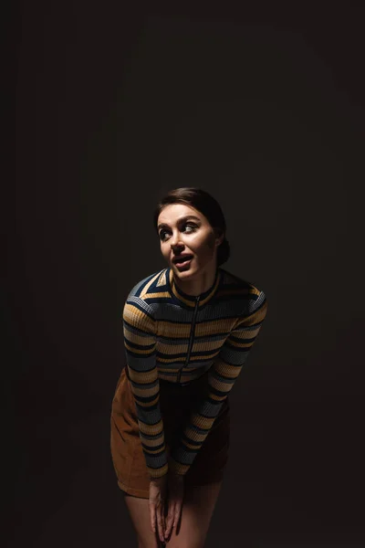 Curious young woman in striped turtleneck with skirt posing isolated on black — Stock Photo