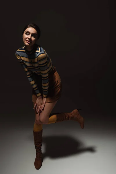 Full length of young woman in autumnal outfit and boots posing on black — Stock Photo