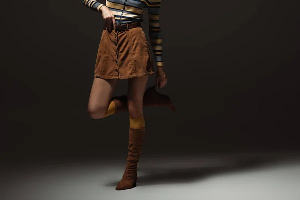 Cropped view of young woman in autumnal outfit and boots standing on black — Stock Photo