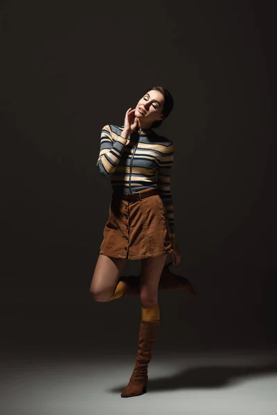 Full length of young woman in turtleneck with skirt and autumnal shoes posing on black — Stock Photo