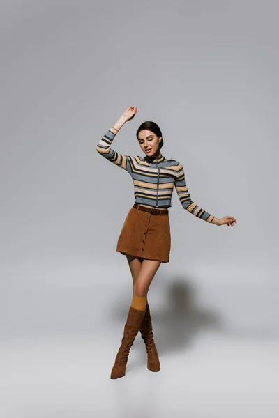 Full length of retro young woman in striped turtleneck with skirt and boots posing on grey — Stock Photo