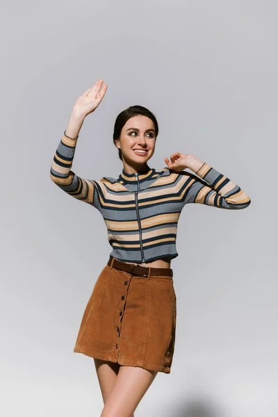Happy young woman in turtleneck and skirt gesturing while posing isolated on grey — Stock Photo