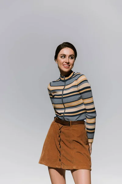 Happy young woman in striped turtleneck and skirt posing isolated on grey — Stock Photo