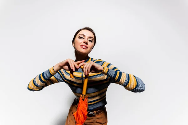 Heureux jeune femme à col roulé rayé posant avec parapluie orange sur blanc — Photo de stock