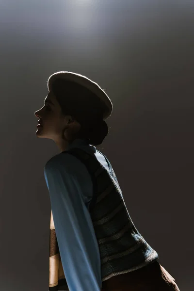 Vue latérale de la jeune femme en béret et tenue automnale sur fond gris foncé — Photo de stock