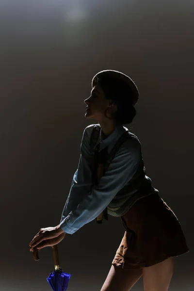 Silhouette of young woman in beret and autumnal outfit on dark grey background — Stock Photo