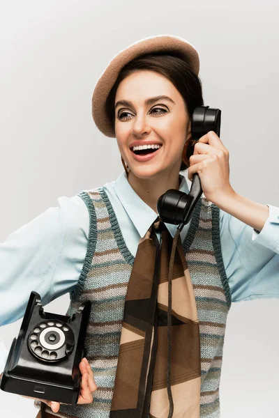 Cheerful young woman in beret talking on vintage telephone isolated on grey — Stock Photo