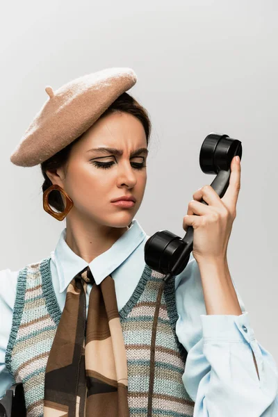 Displeased young woman in beret talking on vintage telephone isolated on grey — Stock Photo