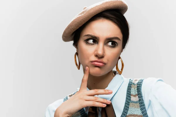 Mujer joven descontenta con maquillaje en boina y chaleco de punto aislado en gris - foto de stock