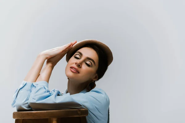 Stylish woman in beret and autumnal clothes leaning on wooden high chair isolated on grey — Stock Photo