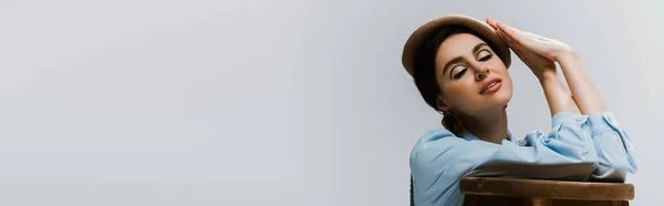 Stylish woman in beret and autumnal clothes leaning on wooden high chair isolated on grey, banner — Stock Photo