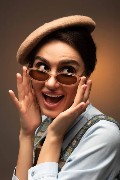 Excitée jeune femme en béret ajuster des lunettes de soleil élégantes sur brun — Photo de stock