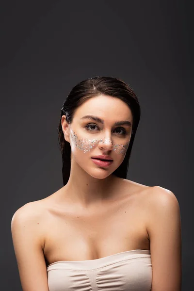 Young woman with bare shoulders and sparkling glitter on cheeks isolated on grey — Stock Photo