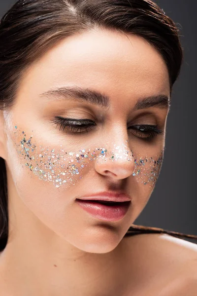 Portrait of young brunette woman with sparkling glitter on cheeks isolated on grey — Stock Photo