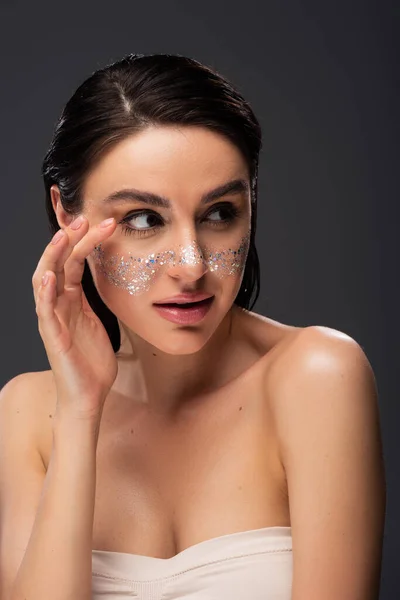 Jolie jeune femme aux épaules nues et aux paillettes scintillantes sur les joues isolées sur gris — Photo de stock