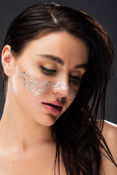 Retrato de mujer morena joven con maquillaje natural y brillo brillante en las mejillas aisladas en gris - foto de stock