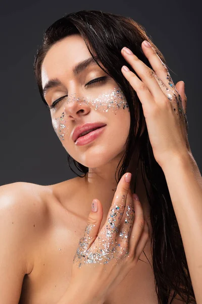 Jeune femme brune avec des paillettes scintillantes sur les joues et les mains isolées sur le gris — Photo de stock