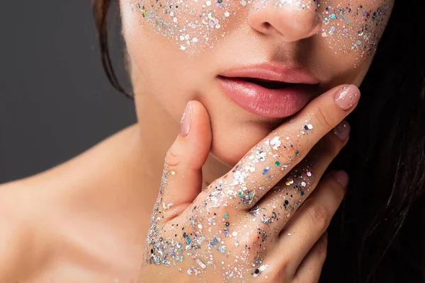 Cropped view of young woman with sparkling glitter on cheeks and hand touching face isolated on grey — Stock Photo