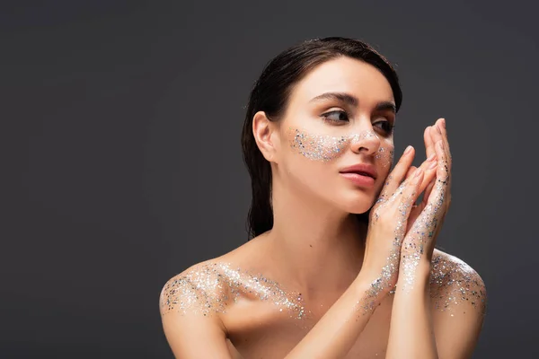 Portrait of young woman with sparkling glitter on cheeks and bare shoulders isolated on grey — Stock Photo