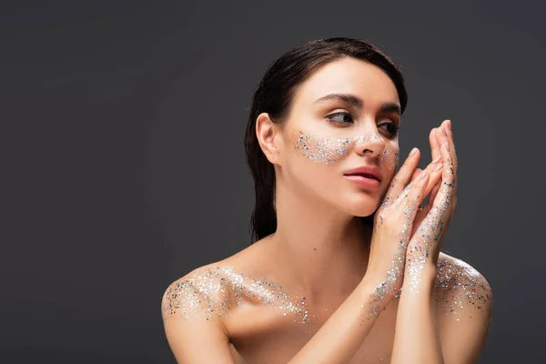 Portrait de jeune femme aux paillettes scintillantes sur les joues et aux épaules nues isolées sur le gris — Photo de stock