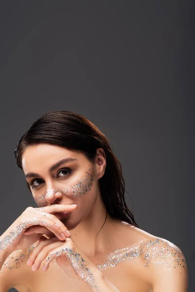 Portrait of young woman with sparkling glitter on cheeks and hands looking at camera isolated on grey — Stock Photo