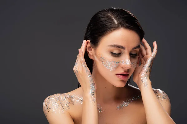 Portrait of young woman with glitter on cheeks and hands adjusting hair isolated on grey — Stock Photo