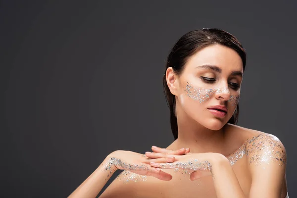 Sensual young woman with clenched hands and sparkling glitter on cheeks isolated on grey — Stock Photo