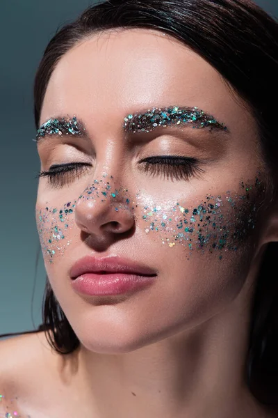 Portrait of young woman with glitter on cheeks and eyebrows isolated on grey — Stock Photo