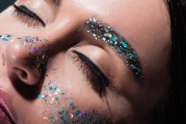 Primer plano de mujer joven con los ojos cerrados y brillo en la cara aislado en gris - foto de stock