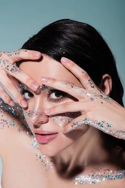 Vue grand angle de la jeune femme avec des paillettes sur le visage et le corps posant isolé sur le gris — Photo de stock